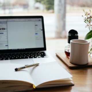 A laptop and notebook sitting on a table beside a cup of coffee.