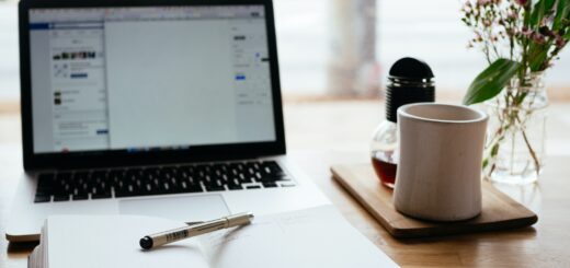 A laptop and notebook sitting on a table beside a cup of coffee.